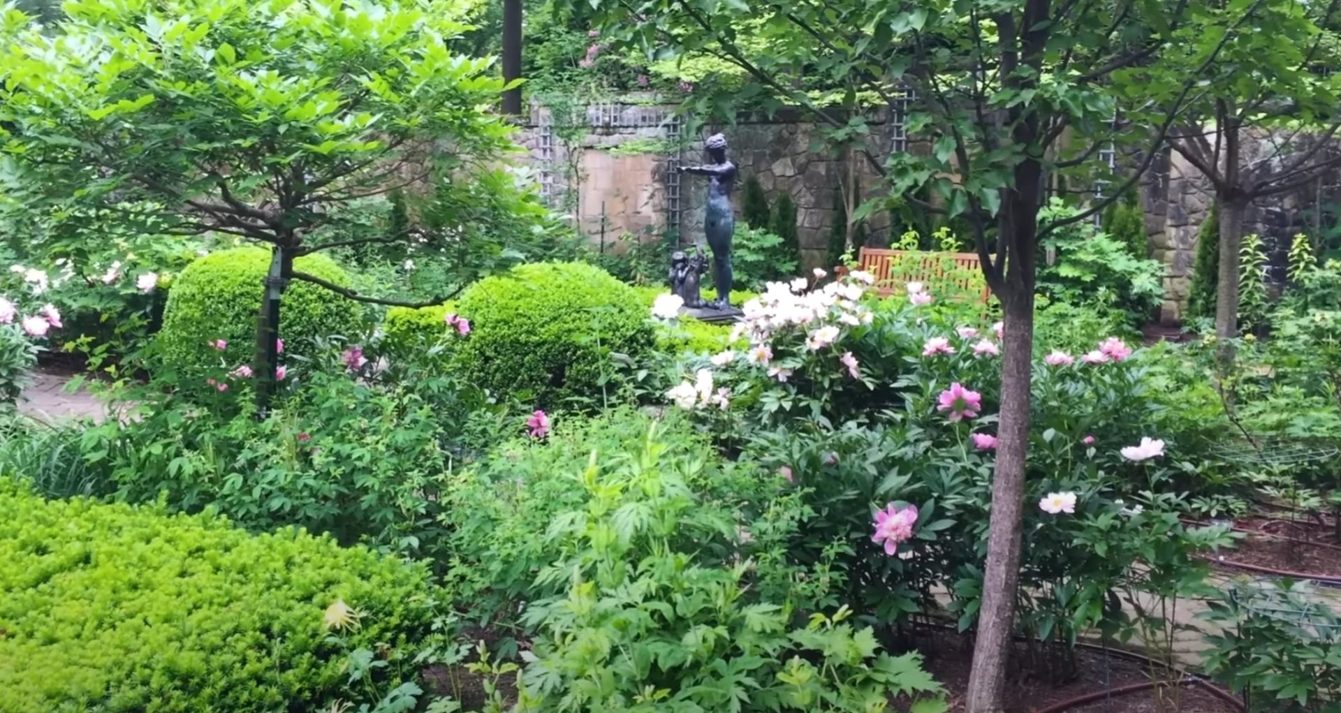 Traditional English garden landscaping with stone walls, mixed perennial flowers, and mature tree canopy
