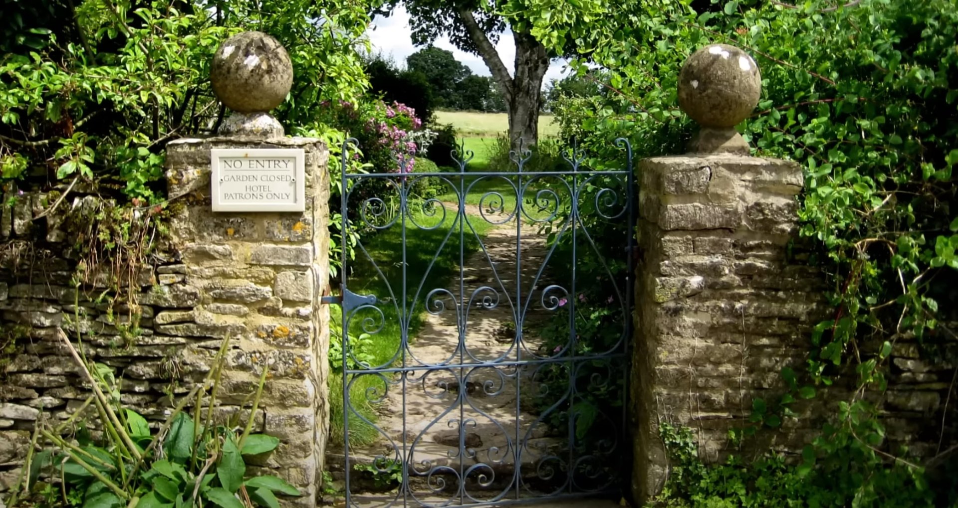 Historic garden entrance with ornate iron gates, stone pillars, and vintage landscaping design elements