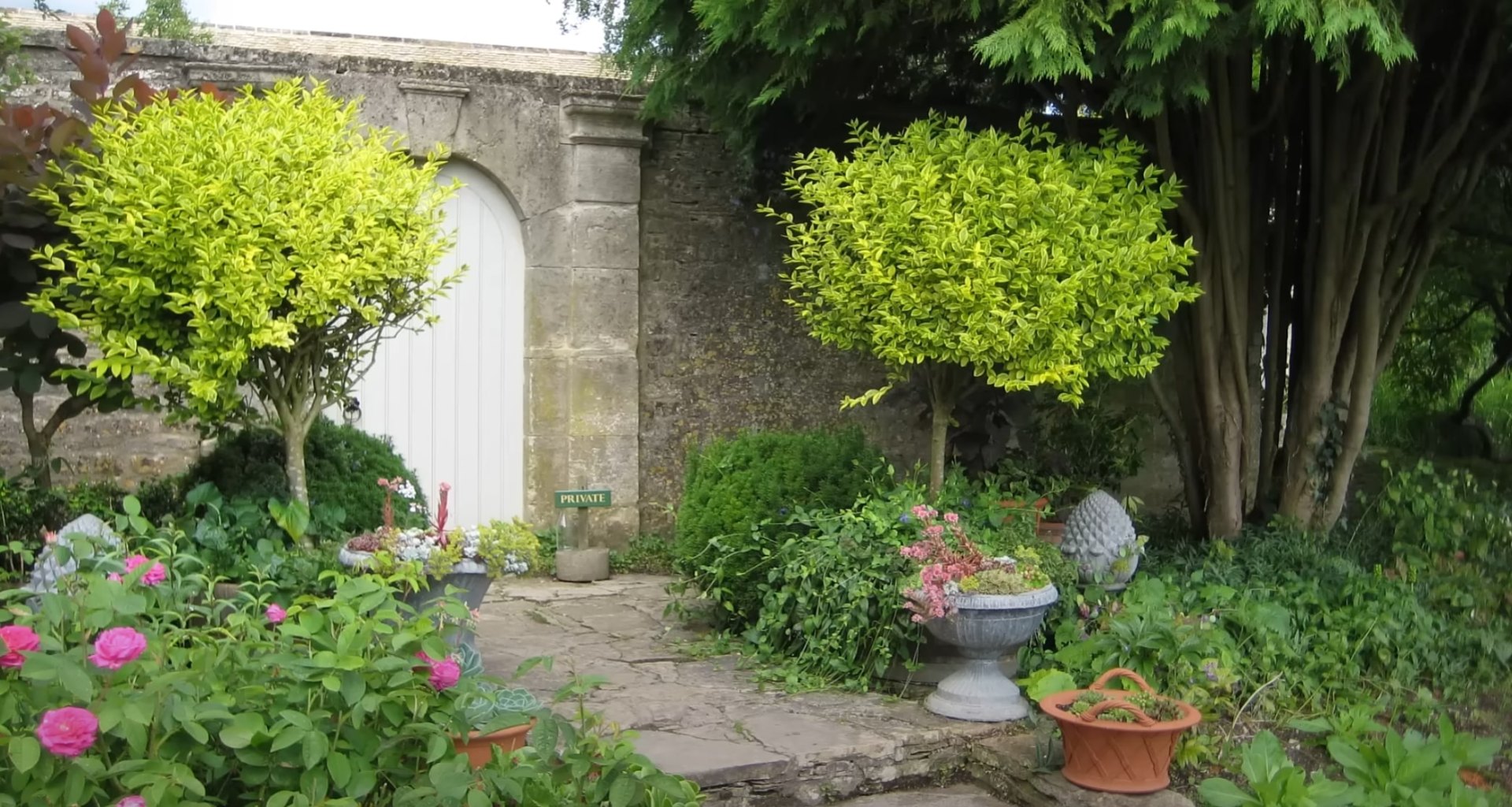 Cottage garden landscaping with stone archway entrance, mixed flowering plants, and traditional paving stones