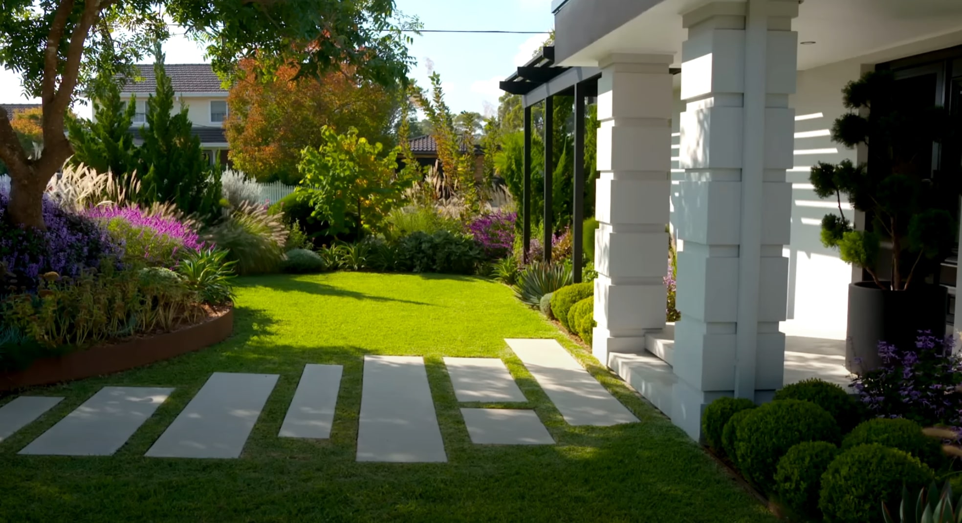 Modern home entrance with concrete paver walkway, purple flowering plants, and professional landscape lighting