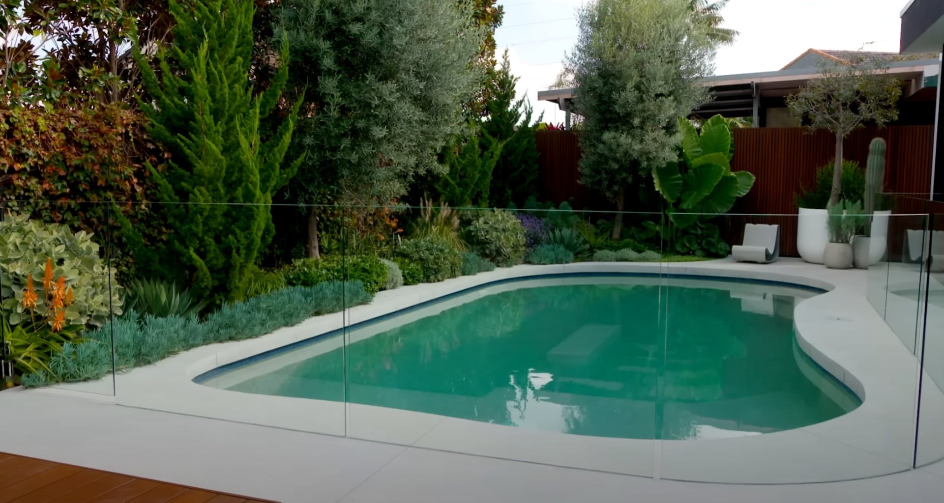 Modern pool area landscaping with lush tropical plants, glass safety fencing, and contemporary outdoor design