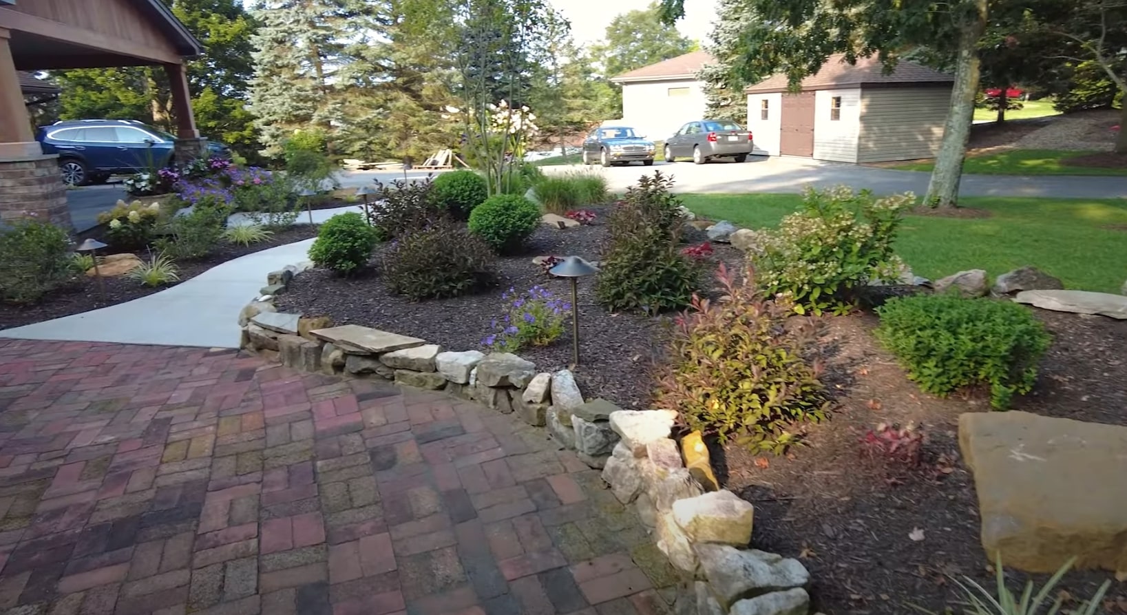 Professional landscaping design featuring curved stone retaining walls, colorful flower beds, and brick paver walkways